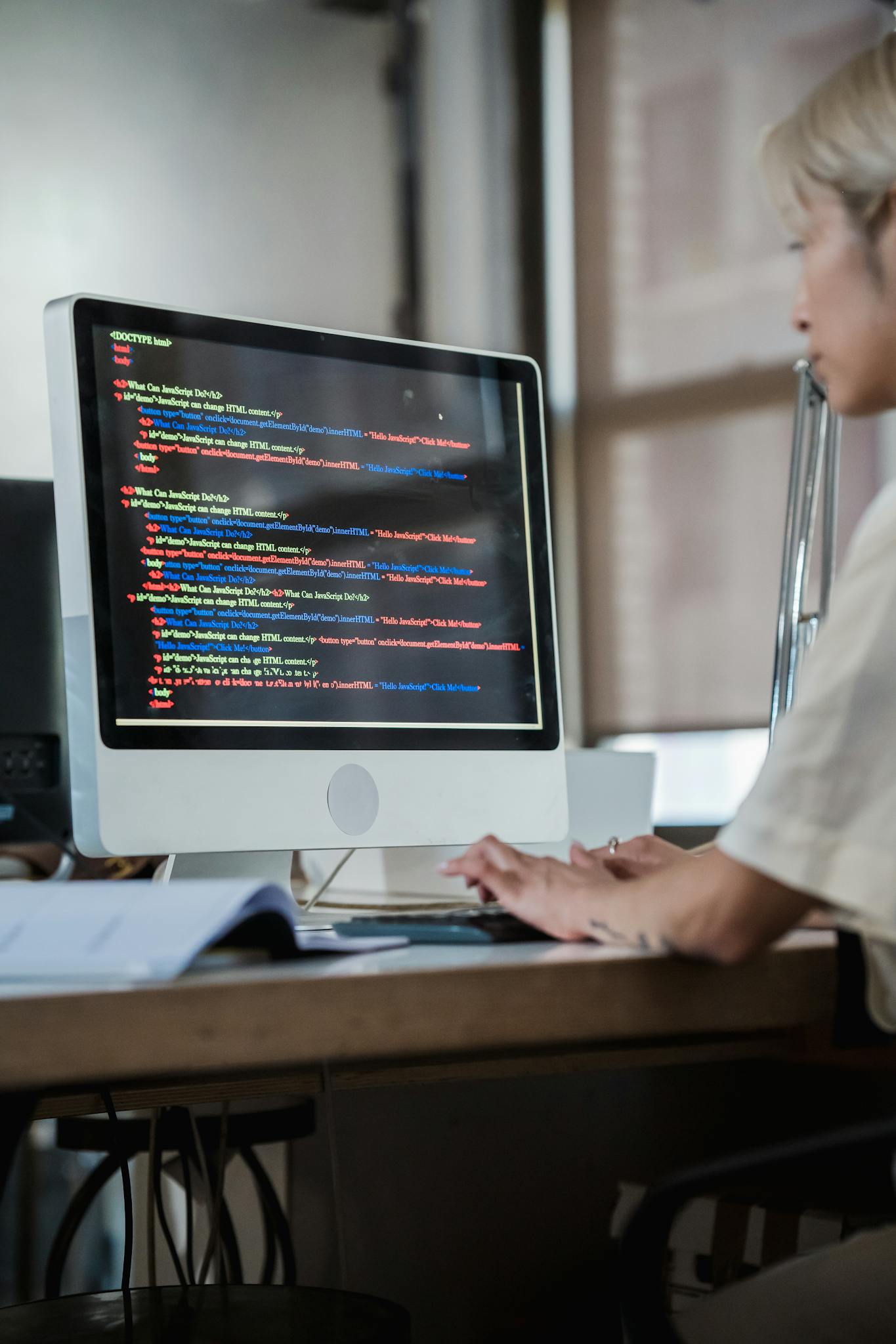 Focused woman working on computer coding in a modern office setting.